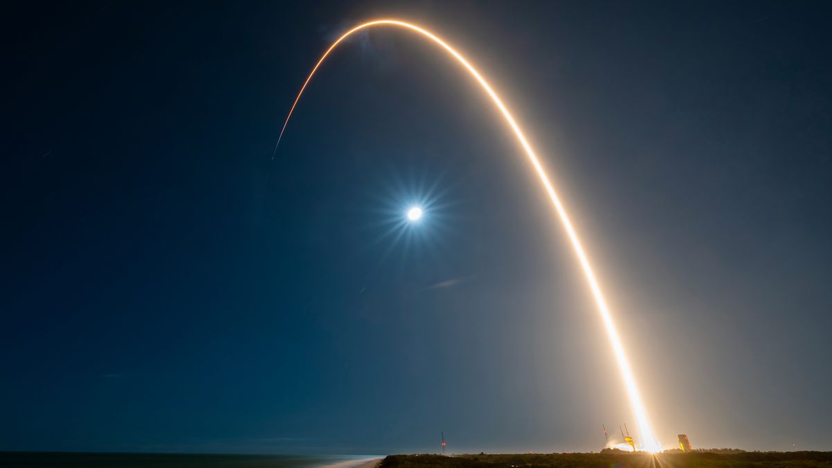 A rocket launch carves an orange arc into a dark night sky in this long-exposure photo.