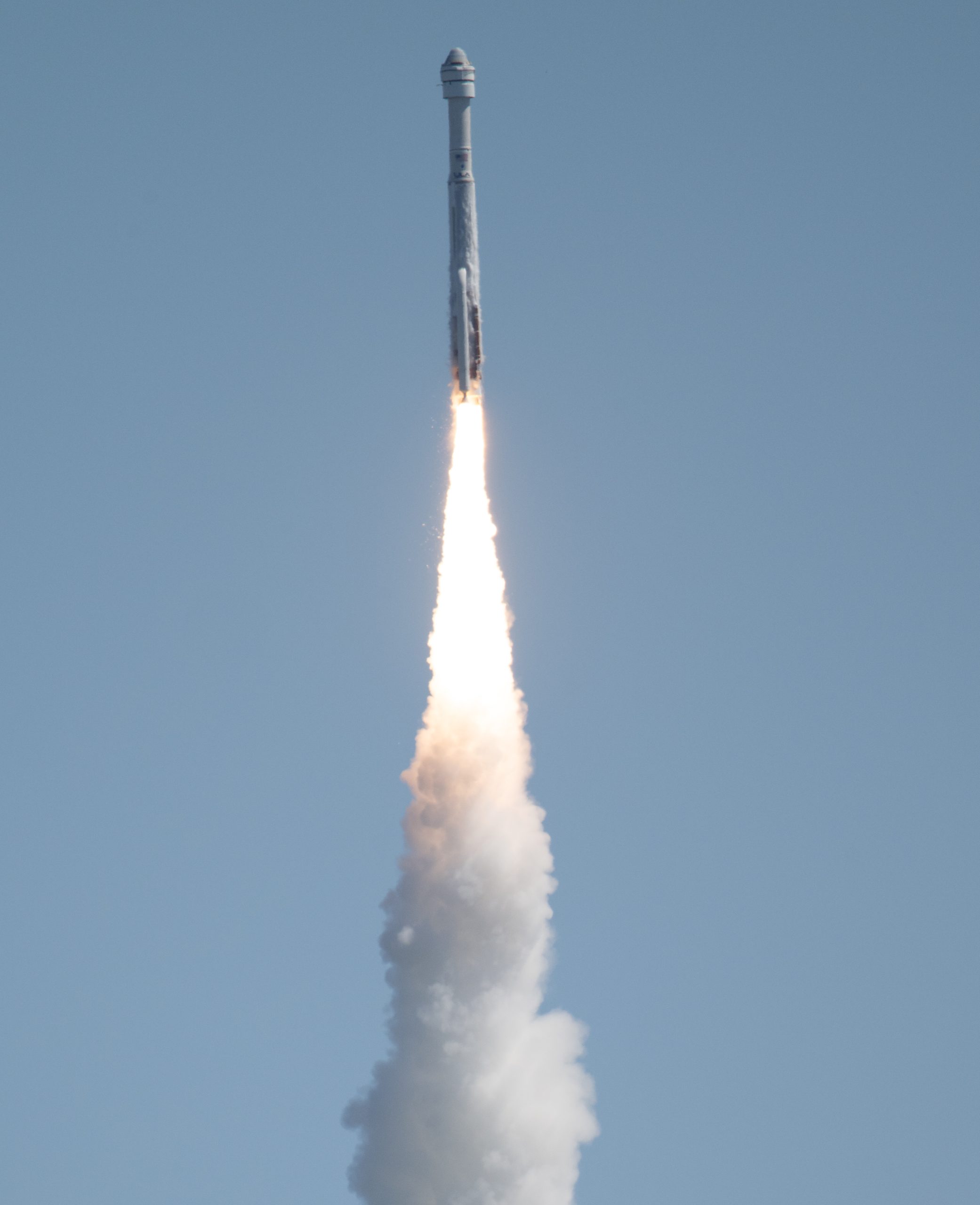 A white rocket takes off, leaving a trail of fire and vapor behind it. The sky is a cool blue-gray.