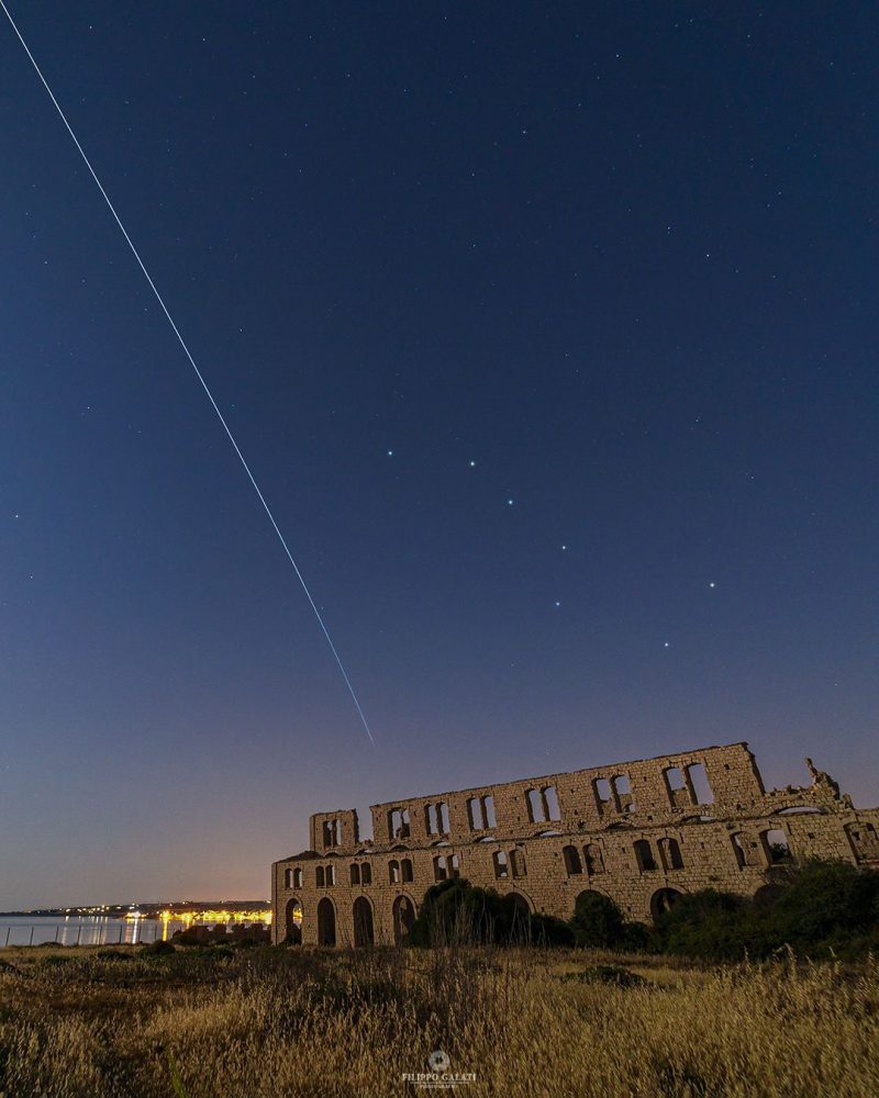 White line in the sky with ancient monument below.