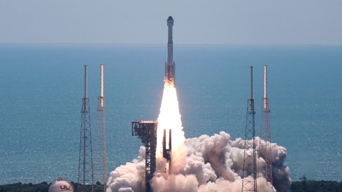 a white rocket launches on a sunny day above a plume of fire and smoke