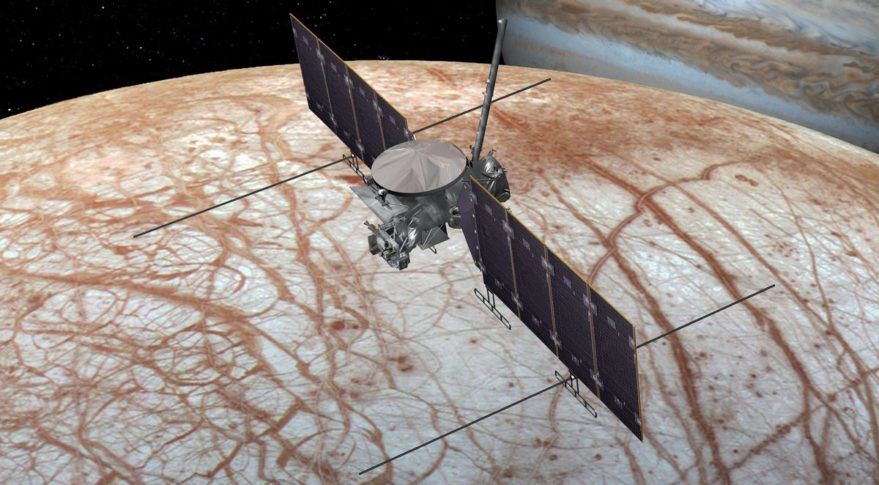 A spacecraft seen over a red-streaked world. Jupiter, a striped and swirly looking world, is in the background, offscreen.